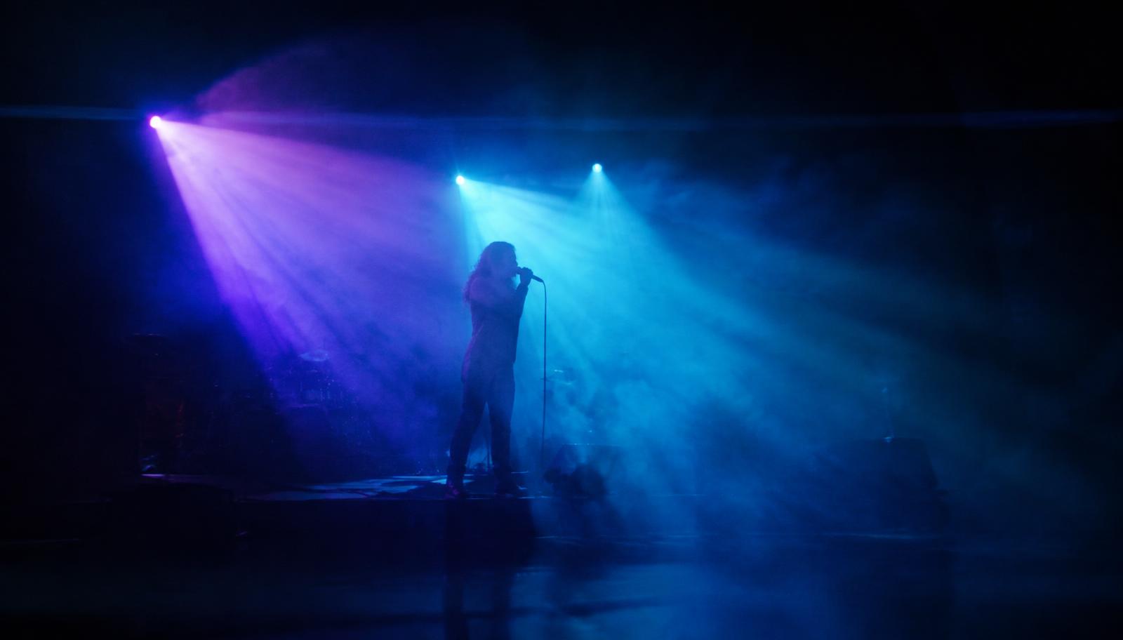 Artista em palco cinematográfico com luzes violeta e ciano